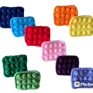May include: Ten crocheted squares in different colours, including blue, green, red, pink, purple, yellow, and orange. Each square has a textured, bumpy surface.