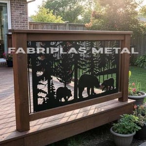 May include: A black metal deck railing panel featuring a laser-cut silhouette of a forest with pine trees and two bears. The panel is mounted within a wooden frame on a deck. The text FABRIPLAS METAL is visible across the center of the panel.