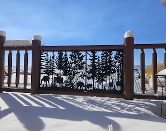 May include: A decorative metal fence panel with a forest scene cut-out. The panel features silhouettes of trees, moose, bears, and deer. The fence is part of a wooden deck covered in snow, with a clear blue sky in the background.