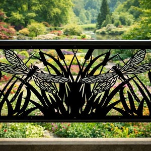 May include: Black metal railing panel featuring a dragonfly design. The panel has two dragonflies with detailed wing patterns, set against a backdrop of reeds and grasses. The railing is installed in front of a garden with colorful flowers and greenery.