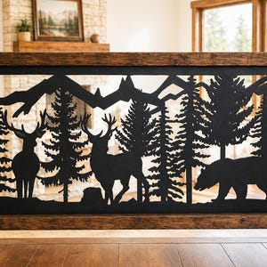 May include: A rectangular black metal railing insert featuring a laser-cut silhouette design of two deer, a bear, pine trees, and mountain peaks. The metal panel is framed by dark brown stained wooden posts and horizontal railing beams.