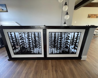 May include: A staircase railing featuring two rectangular panels with a black metal cutout design of a dense pine forest. The panels are framed in white and set within a dark brown wooden structure, creating a decorative barrier for the stairs.