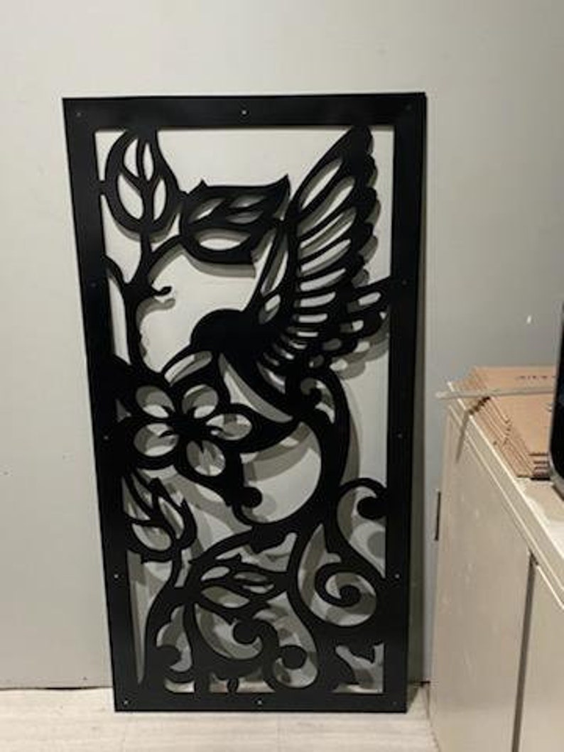 May include: Black metal wall decor featuring a hummingbird in flight with intricate floral details. The design is cut out of the metal, creating a delicate and airy look.