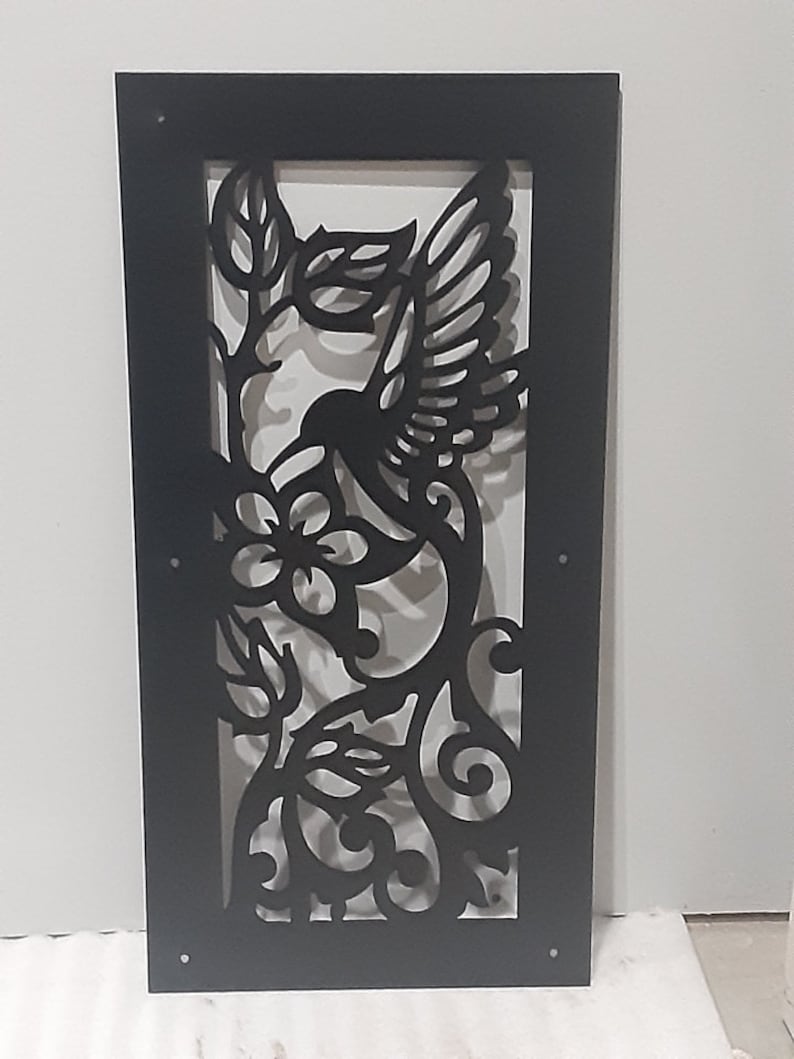 May include: Black metal wall decor featuring a hummingbird in flight with intricate floral details. The hummingbird is depicted with outstretched wings and a long beak, hovering near a stylized flower.