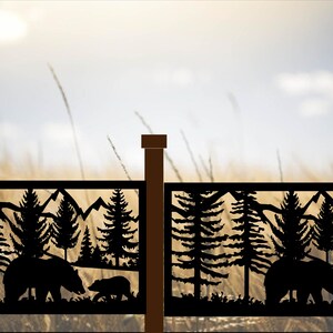 May include: Black metal fence panels with a nature scene featuring bears, trees, and mountains. The silhouettes are set against a blurred background of a field and sky. The fence posts are brown.