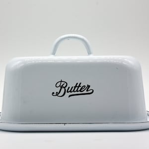 May include: White enamel butter dish with a black handle and the word "Butter" in black script on the lid.