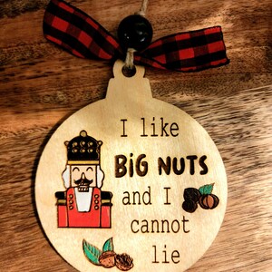 May include: A wooden Christmas ornament shaped like a circle with a nutcracker illustration and the text "I like big nuts and I cannot lie".