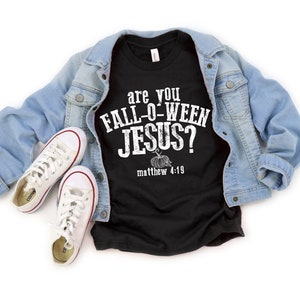 May include: Black t-shirt with the text "are you FALL-O-WEEN JESUS?" and "matthew 4:19" in white. The shirt is paired with a light blue denim jacket and white canvas sneakers with red trim.