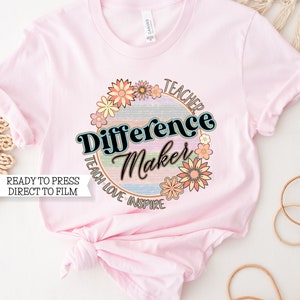 May include: Pink t-shirt with a round graphic design featuring a rainbow background, the text "Teacher Difference Maker", and a floral border. The text "Teach Love Inspire" is written around the circle.