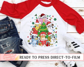 May include: A white and red raglan-style shirt featuring a Christmas-themed graphic. The graphic includes cartoon dogs wearing Santa hats and surrounded by Christmas lights and a decorated tree. The text "READY TO PRESS DIRECT-TO-FILM" is at the bottom.