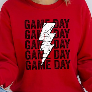 May include: Red sweatshirt with a white lightning bolt graphic and the text "GAME DAY" repeated five times.