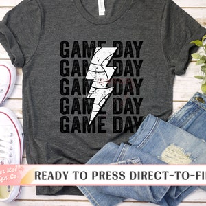 May include: A dark grey t-shirt with a white lightning bolt and the text "GAME DAY" repeated five times. The text is in a distressed font. The shirt is ready to press with direct-to-film.