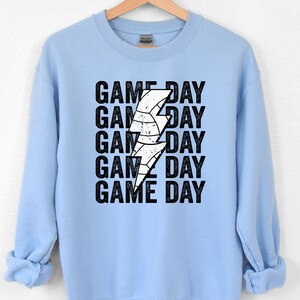 May include: Light blue sweatshirt with a white lightning bolt graphic and the text "GAME DAY" repeated five times.