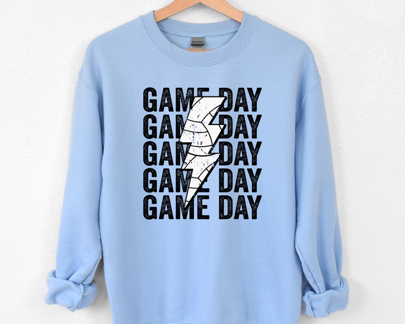 May include: Light blue sweatshirt with a white lightning bolt graphic and the text "GAME DAY" repeated five times.
