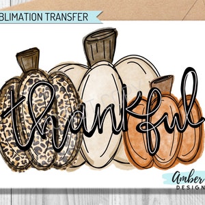 May include: A watercolor design featuring three pumpkins with the word "thankful" in a handwritten font. The pumpkins are in shades of brown, cream, and orange, with one pumpkin displaying a leopard print pattern. The words "Sublimation Transfer" are at the top.