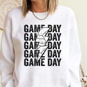 May include: White sweatshirt with black text that reads "GAME DAY" repeated five times. A black and white lightning bolt graphic with a basketball inside is centred between the words.