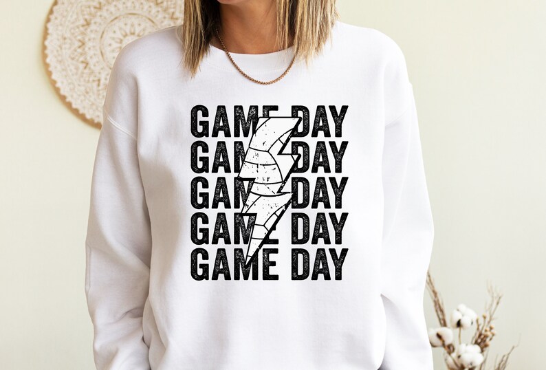 May include: White sweatshirt with black text that reads "GAME DAY" repeated five times. A black and white lightning bolt graphic with a basketball inside is centred between the words.