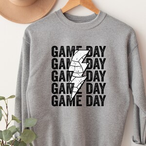 May include: Grey sweatshirt with a white lightning bolt graphic and the text "GAME DAY" repeated five times.