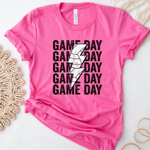 May include: Pink t-shirt with a black and white lightning bolt graphic and the text "GAME DAY" repeated five times.