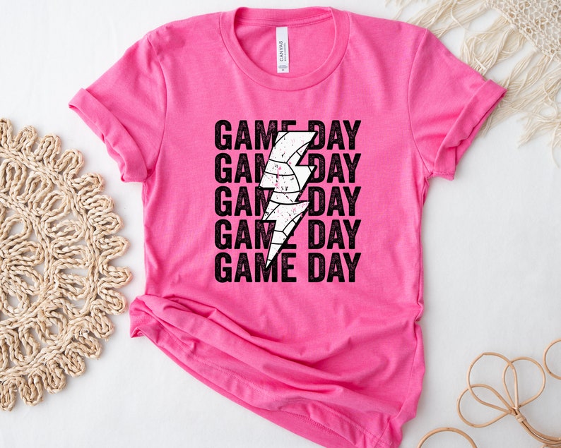 May include: Pink t-shirt with a black and white lightning bolt graphic and the text "GAME DAY" repeated five times.