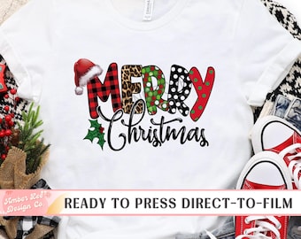 May include: White t-shirt with a festive "Merry Christmas" design. The text features a Santa hat, plaid, leopard print, polka dots, and holly. The phrase "READY TO PRESS DIRECT-TO-FILM" is printed at the bottom.