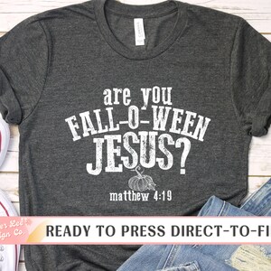 May include: Dark gray t-shirt with the text "are you FALL-O-WEEN JESUS?" in distressed white lettering. A pumpkin graphic is below the text, with "matthew 4:19" underneath. The shirt is displayed with jeans and sneakers.
