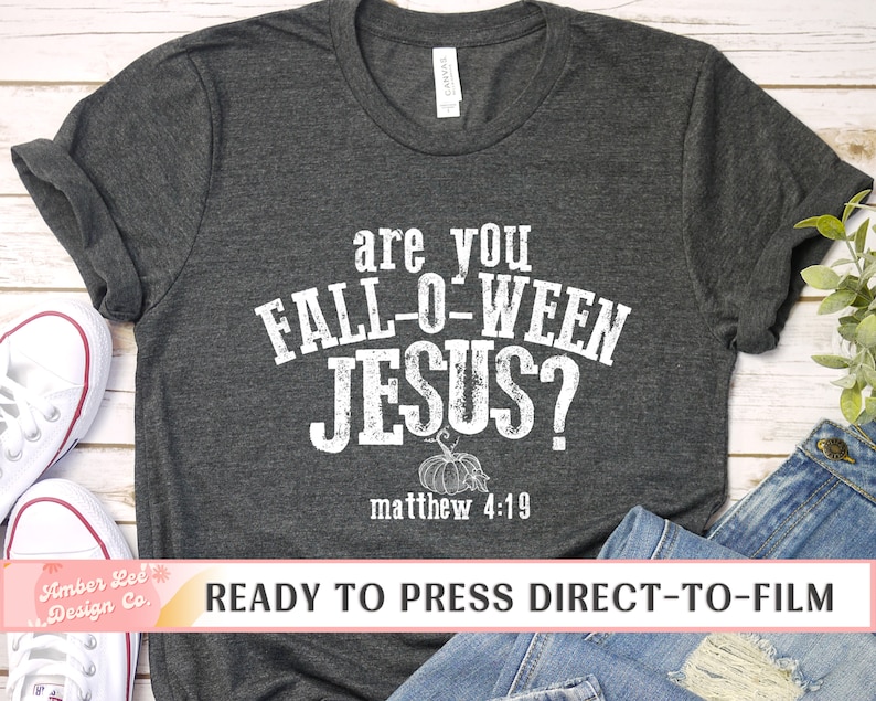 May include: Dark gray t-shirt with the text "are you FALL-O-WEEN JESUS?" in distressed white lettering. A pumpkin graphic is below the text, with "matthew 4:19" underneath. The shirt is displayed with jeans and sneakers.