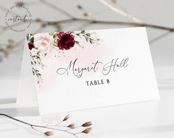 May include: A white place card with a pink and burgundy floral design. The text "Margaret Hall" and "Table 8" is printed in black.