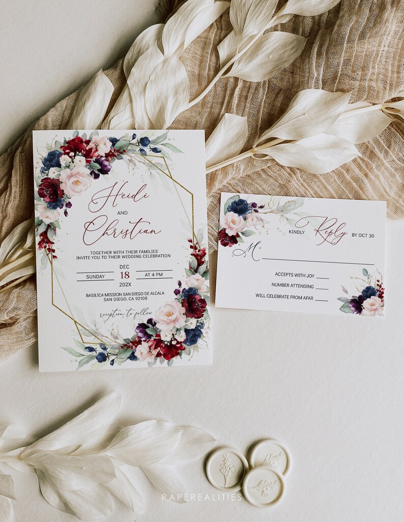 May include: Wedding invitation with a gold geometric frame and floral design. The invitation features burgundy, pink, and blue flowers with green leaves. The text reads "Heidi and Christian" and includes the date and time of the wedding ceremony. The RSVP card features a similar floral design and includes a space for guests to indicate their attendance.