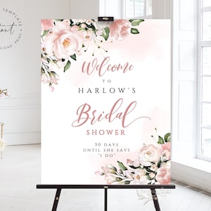Op de afbeelding: Een wit welkomsbord voor een bruiloft met roze aquarelbloemen en de tekst "Welkom op de bruiloft van Harlow 30 dagen tot ze "Ja" zegt"
