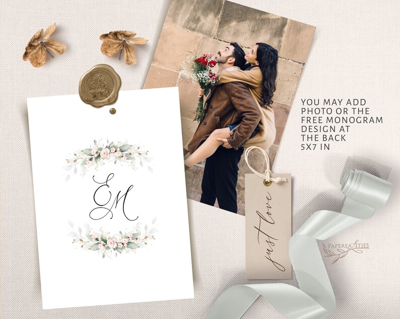 May include: A white card with a watercolour floral wreath and the initials "EM" in black calligraphy. The card is 5x7 inches and can be personalised with a photo or monogram. The text "just love" is written on a small brown tag.