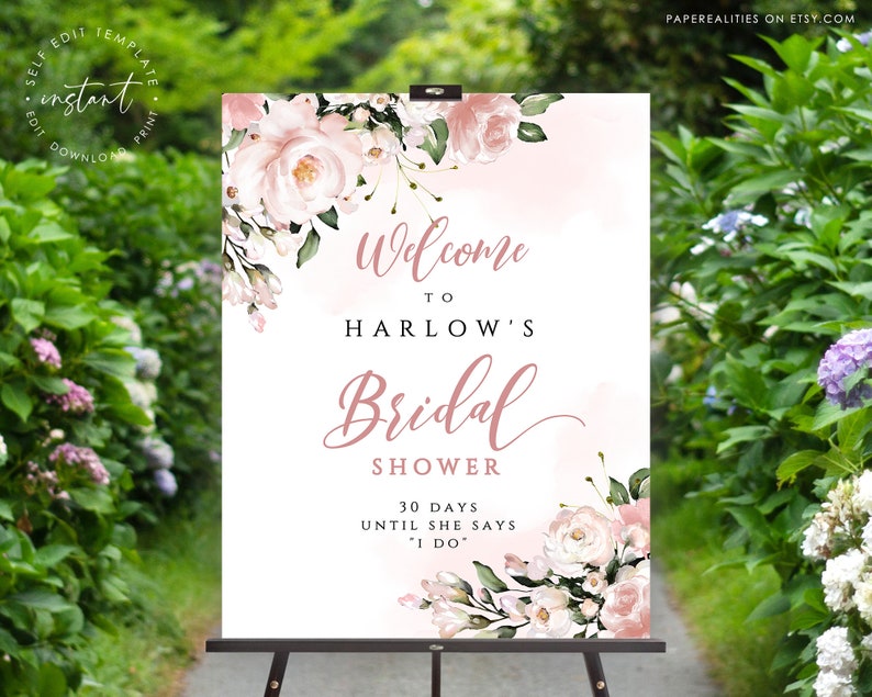 Op de afbeelding: Een wit welkomsbord voor een bruiloft met roze aquarelbloemen en de tekst "Welkom op de bruiloft van Harlow 30 dagen tot ze "Ja" zegt"
