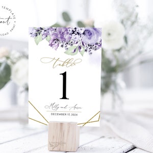 May include: Purple and green floral wedding table number card with gold geometric accents. The card reads "Table 1" and includes the names "Molly and Arm" and the date "December 17, 202X".
