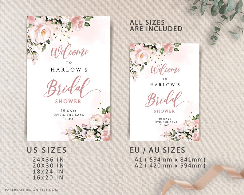 Op de afbeelding: Een afdrukbaar bruiloftsshowerbord met roze bloemenontwerpen en de tekst "Welkom bij Harlow's Bridal Shower 30 dagen tot ze 'Ja' zegt" Het bord bevat US en EU/AU maten in inches en millimeters.