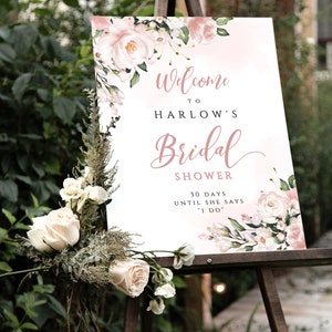 Op de afbeelding: Een wit bord met roze bloemenaccenten en de tekst "Welkom bij Harlow's Bridal Shower 30 dagen tot ze "Ja" zegt"