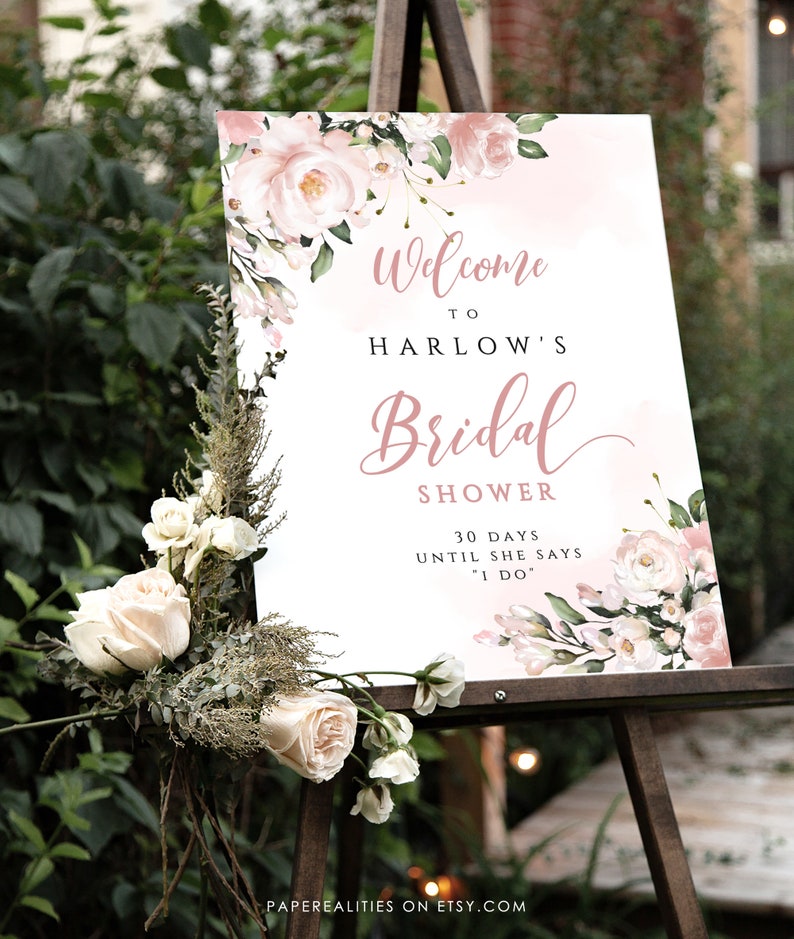 Op de afbeelding: Een wit bord met roze bloemenaccenten en de tekst "Welkom bij Harlow's Bridal Shower 30 dagen tot ze "Ja" zegt"