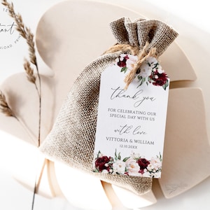 May include: A white wedding favor tag with burgundy and white floral illustrations. The tag says "thank you" for celebrating our special day with us with love, Vittoria & William, 12.10.20XX.