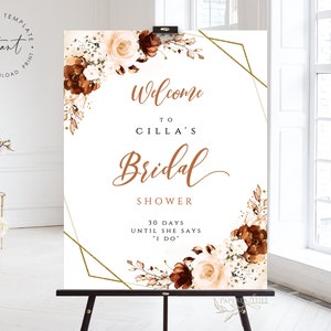 Könnte beinhalten: Ein weißes Willkommens-Schild für eine Brautparty mit goldenen geometrischen Formen und braunen floralen Akzenten. Der Text lautet "Willkommen zur Brautparty von Cilla 30 Tage bis sie 'Ja' sagt".