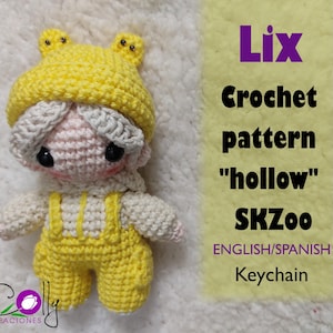 May include: A crocheted doll in a yellow frog hat and dungarees. The doll has a pink face, black eyes, and a cream-coloured outfit. The image includes text that reads "Lix Crochet pattern 'hollow' SKZoo ENGLISH/SPANISH Keychain."