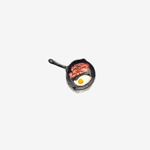 May include: A black cast iron skillet with a single fried egg and bacon strips.