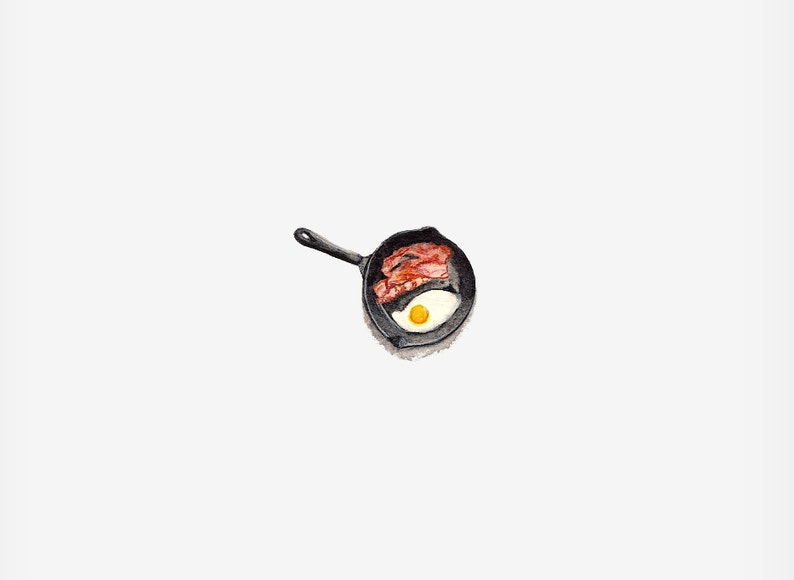 May include: A black cast iron skillet with a single fried egg and bacon strips.