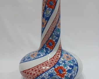 May include: A white ceramic vase with a swirling design of red, blue, and green flowers. The vase has a wide base and a narrow neck.