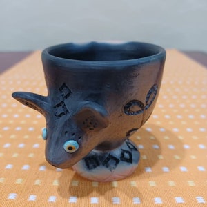 以下が含まれることがあります： 青い目をしたスタイリッシュな動物の形をした黒いセラミック製の卵カップ。カップは、幾何学模様のテクスチャ加工が施されています。