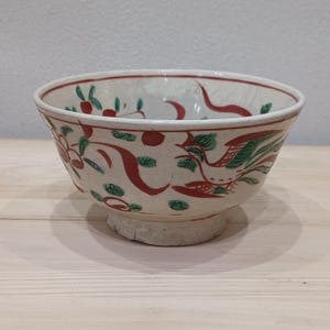 Puede incluir: Un cuenco de cerámica blanca con un diseño floral rojo y verde. El cuenco tiene un borde ancho y un pie pequeño.