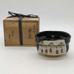 May include: A black and white tea bowl with a brown design. The bowl is in a wooden box with Japanese characters on the side. The characters read "黒田 窯".