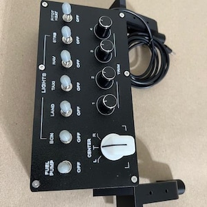 May include: A black flight simulator control panel featuring a column of seven toggle switches labeled for lights and fuel pump, four black rotary trim knobs, and one large white center dial. The unit includes a black cable and mounting bracket.