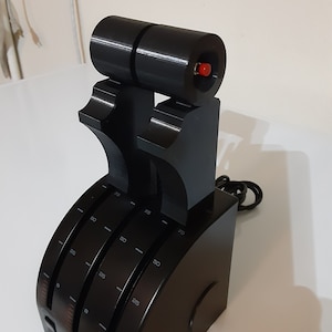 Op de afbeelding: Zwart throttle quadrant met drie knoppen en een rode knop. De knoppen zijn gemarkeerd van 0 tot 75.