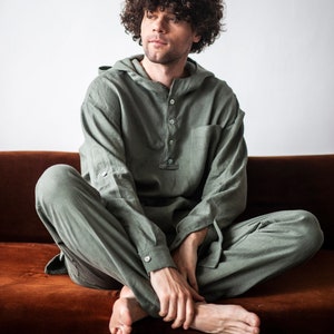 May include: A person wearing a green hooded linen jumpsuit, sitting on a brown couch. The person has curly brown hair and is looking to the side.
