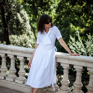 Medium length white linen dress with front wrap panels and a notched collar.