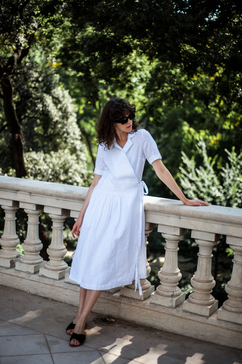 Medium length white linen dress with front wrap panels and a notched collar.